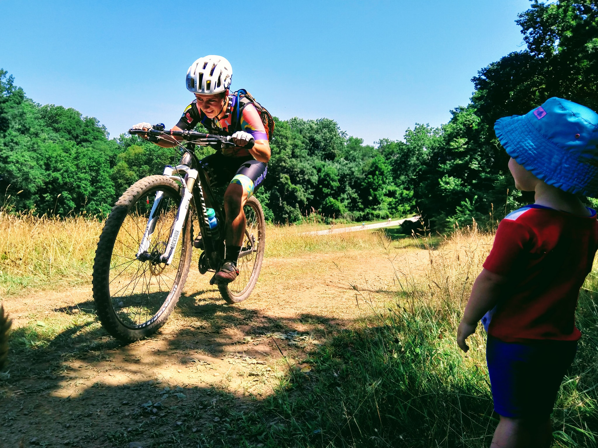 Caitlin on a mountain bike, smiling as she rides past a young child.